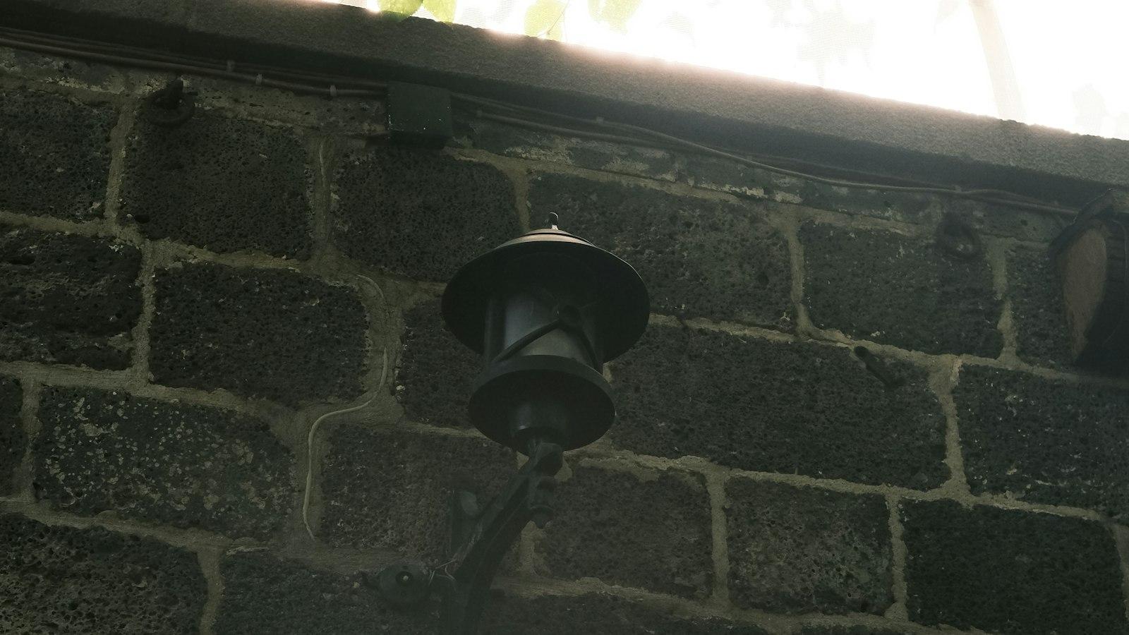 Outdoor lamp fixed to a brick compound wall under a tree