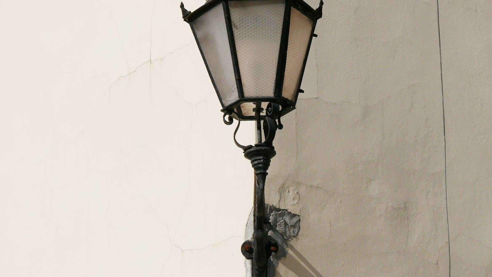 Black wall lantern on a tall upright arm against a pale plastered facade